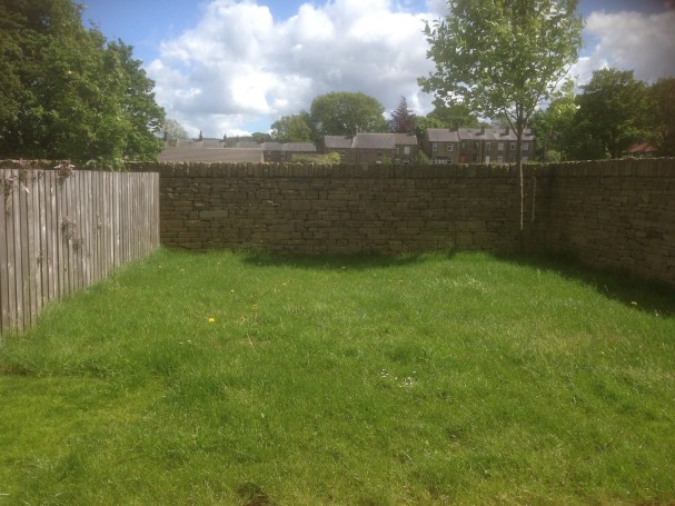 Large garden with patio overlooking green fields.